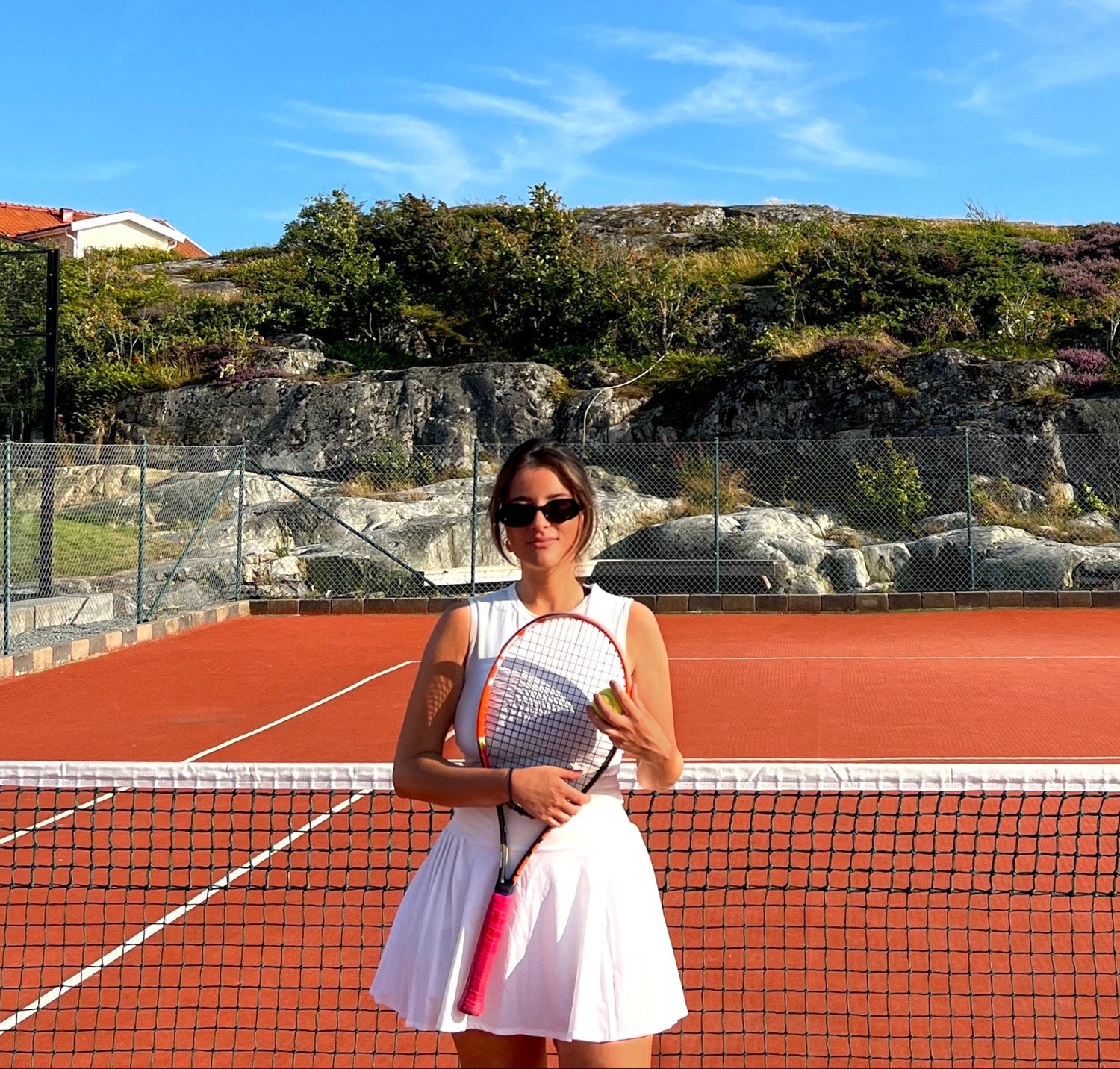 Community Lead for Net Socials, social tennis community and club based in Sweden and London. Woman holding a tennis racket on a tennis court with a scenic background